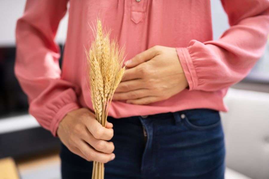 donna che si tiene la pancia perchè ha dolore con una spiga di grano in mano