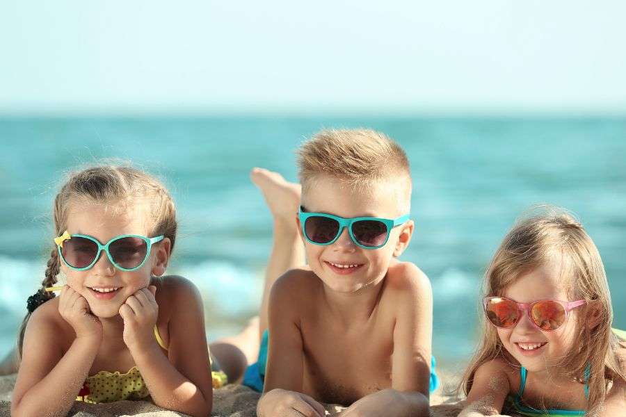 bambini al mare con occhiali da sole che si divertono sul bagnasciuga