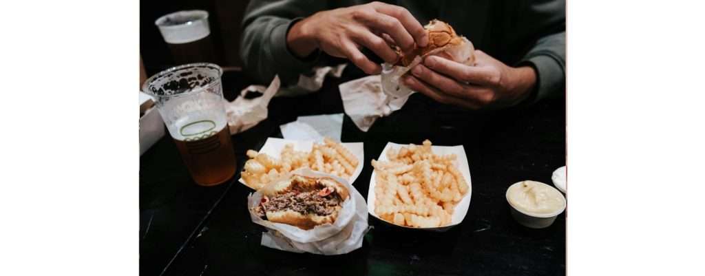 uomo che mangia cibo poco salutare come patatite fritte e hamburger