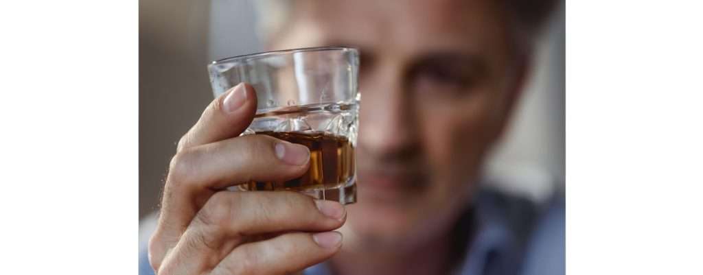 uomo che beve un bicchiere di superalcolico