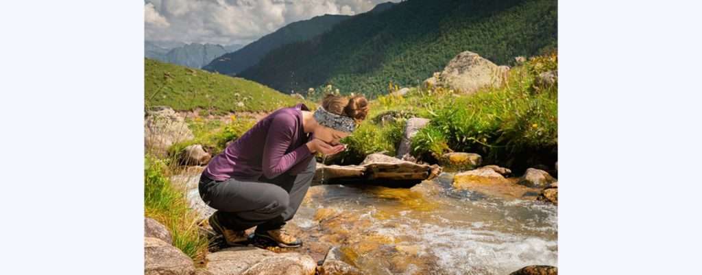 Anche l'acqua di torrente, se contaminata, può provocare la giardiasi, donna che beve dal torrente
